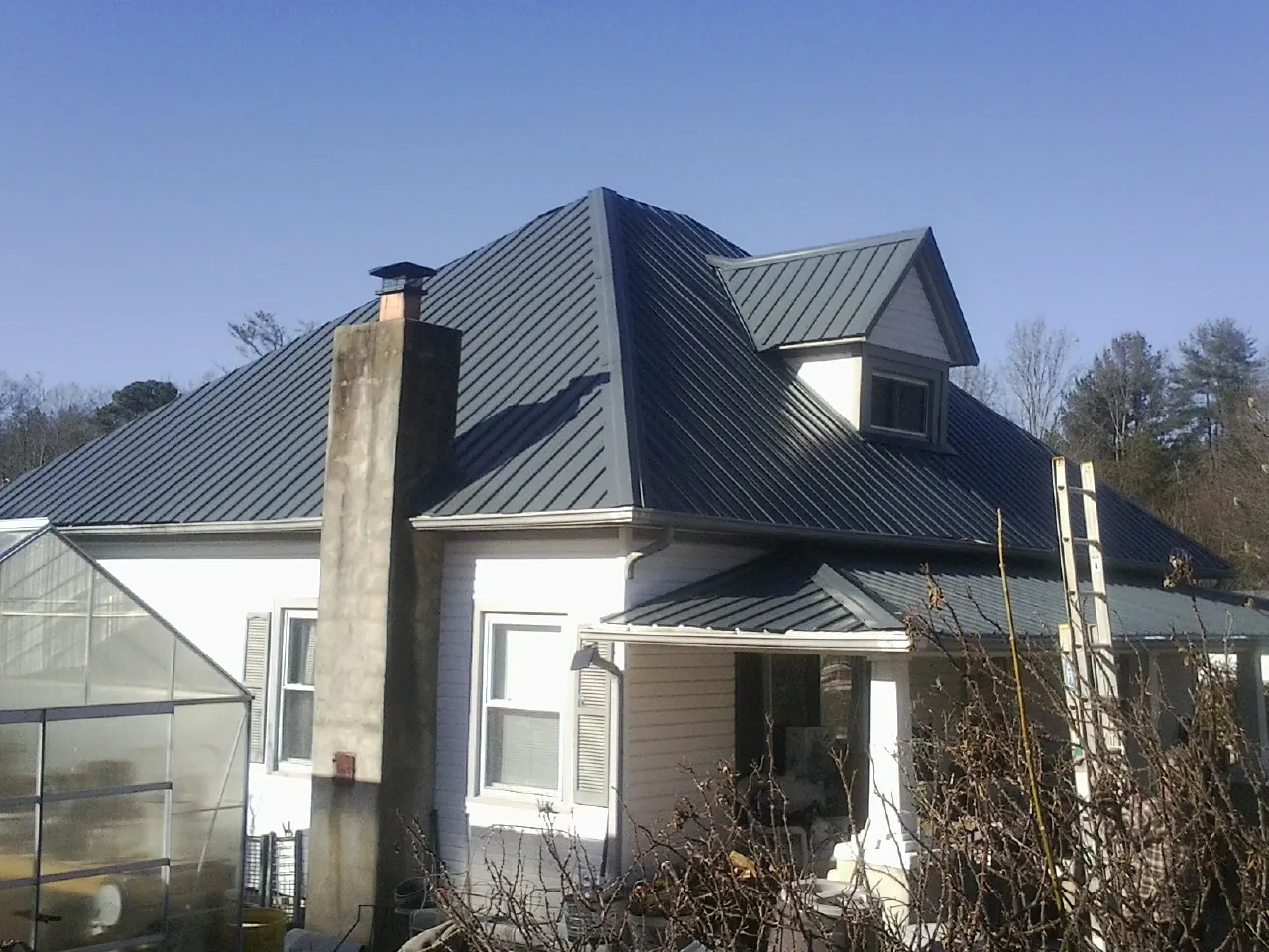 Dark blue standing seam metal roof on a white farmhouse with dormer — Slate & Tile Roof Repair by Roofing Brothers in Blakely