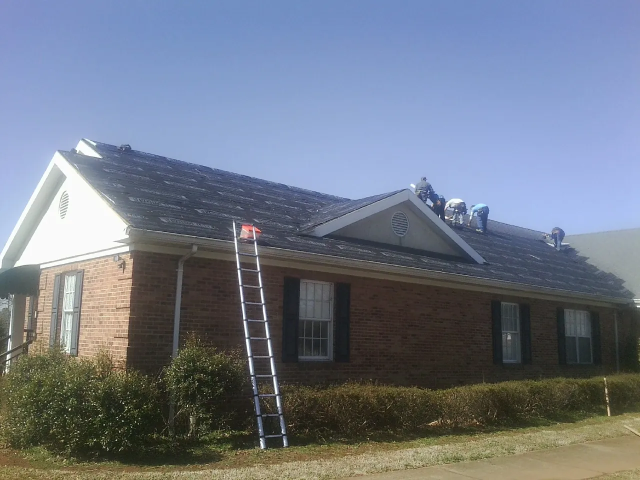 Crew tearing shingles off a brick ranch roof with a ladder set — Emergency Roof Repair work by our crew in Blakely