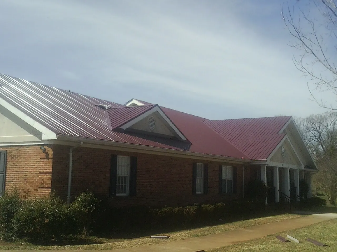 Red metal roof with gabled entries on a long brick building, from a Hail Damage Roof Repair job in Blakely