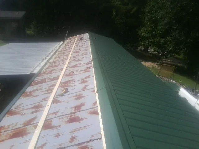 Old rusted panels beside newly installed green metal roofing — Wind Damage Roof Repair by Roofing Brothers in Blakely