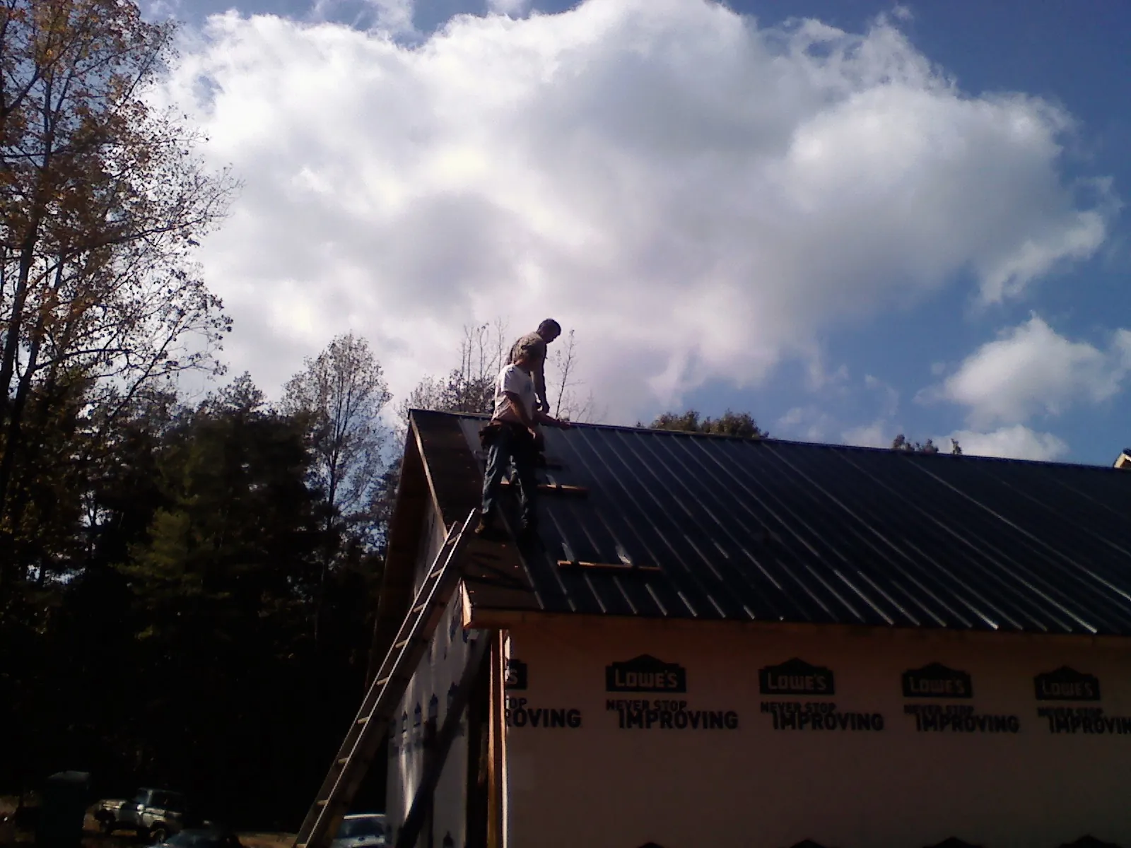 Roofer fastening dark metal panels high against a cloudy sky, from a Roof Inspection job in Blakely