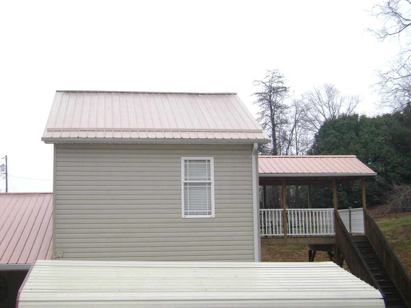 Tan metal roofs on a two story addition and attached porch, from a Roof Replacement job in Blakely